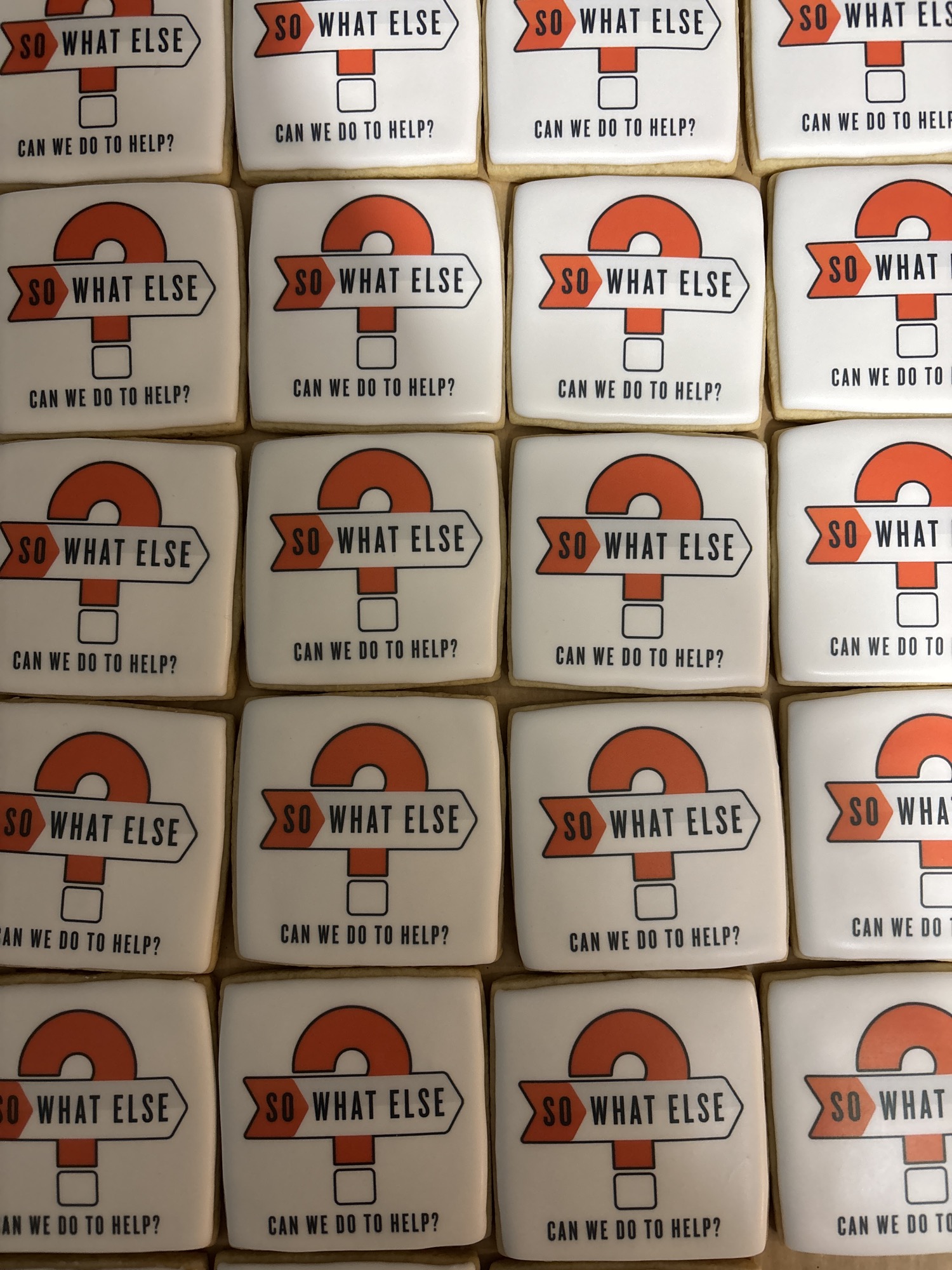 Square white cookies printed with a nonprofit logo: an orange question mark behind a signpost, with a line of text beneath.