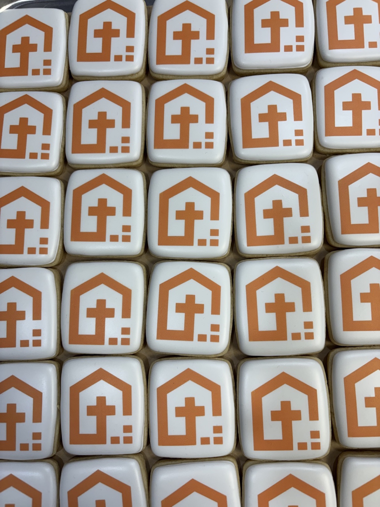 Small square white cookies printed with an orange house-and-cross emblem, laid out in rows.