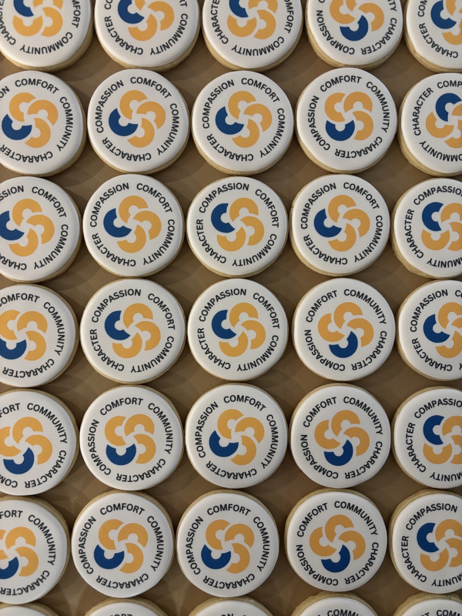 Round white cookies printed with a blue and gold pinwheel emblem ringed by the words compassion, comfort, community and character.